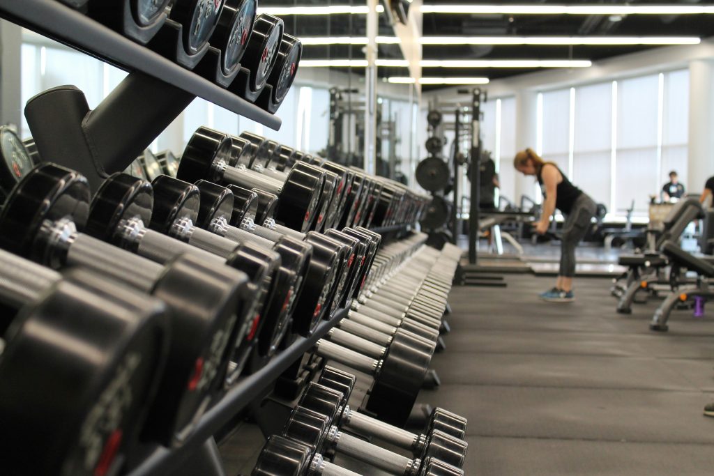 Dumbbells on a rack at a gym with a woman in the background working out