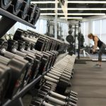 Dumbbells on a rack at a gym with a woman in the background working out